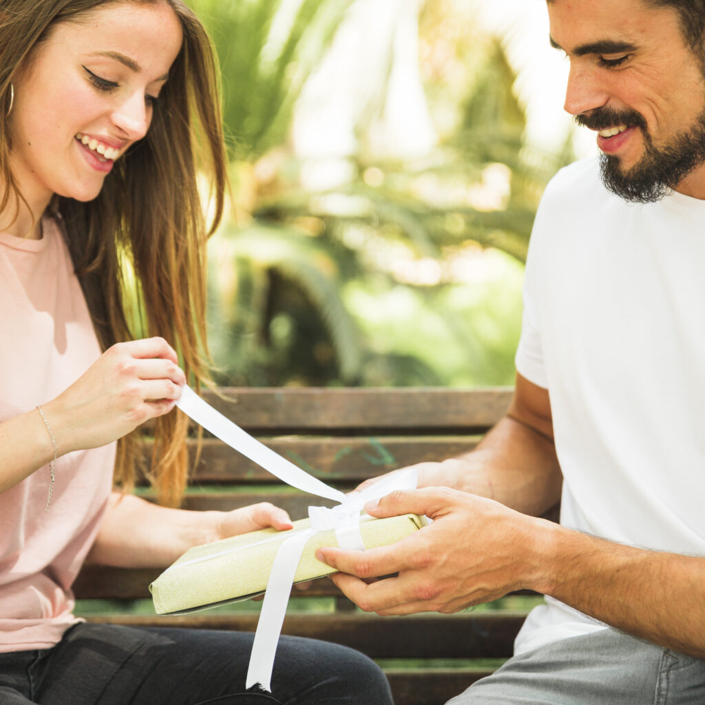Smiling Young Woman Unwrapping Gift Bought By Her Boyfriend